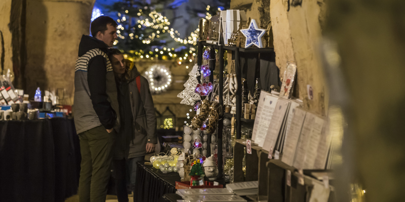 Jonge vrouw heeft hoofd op schouder van jongeman terwijl ze kijken naar kerstartikelen in kerstmarkt Fluweelengrot